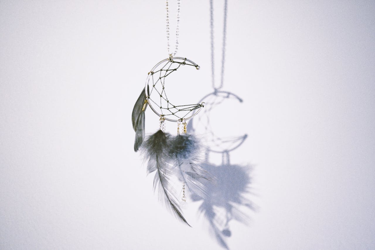 A decorative dreamcatcher with feathers casting a shadow on a white wall.