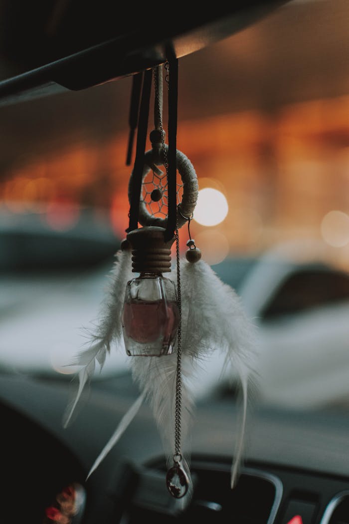 Artistic shot of a handcrafted dreamcatcher with feathers and a bottle hanging inside a car.