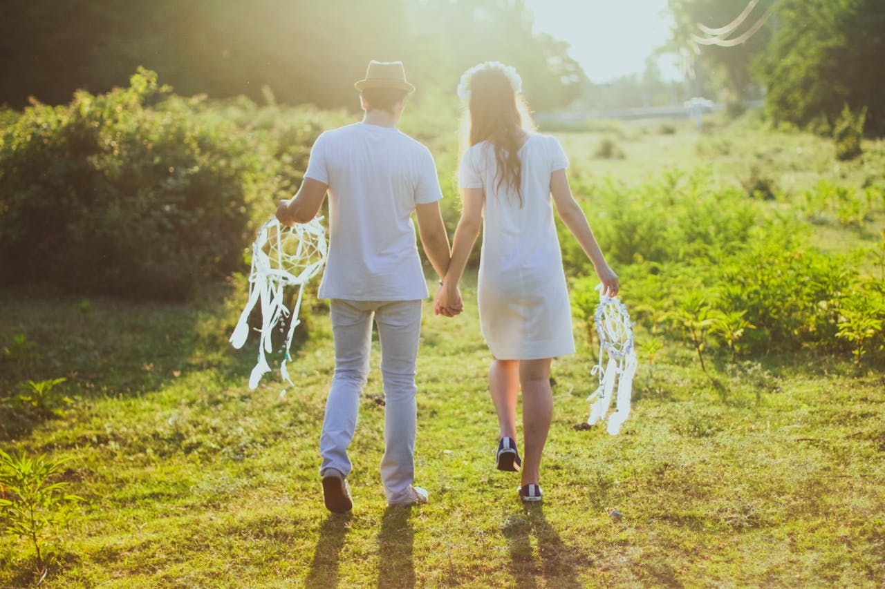 Couple walking hand in hand in a sunny field, holding decorations.